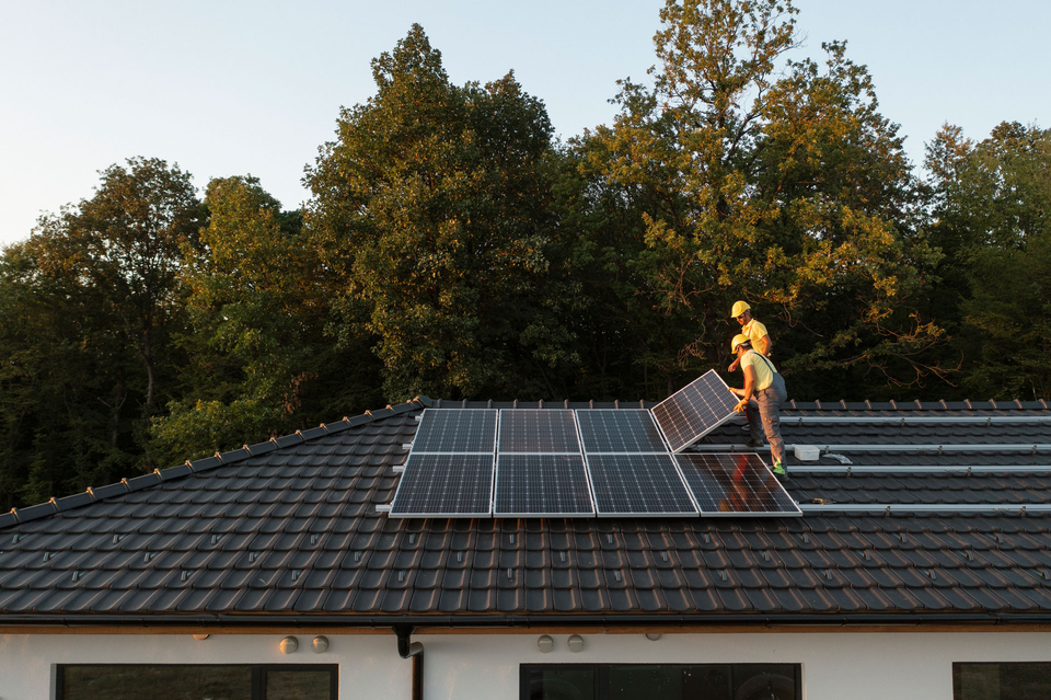 Two Professionalists Installing Solar Panels On A  Roof Of A Modern House.