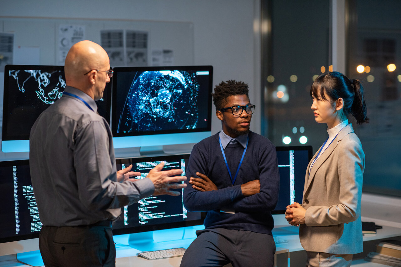 Three intercultural colleagues in formalwear discussing working points at meeting by their workplace in openspace office | © pressmaster (Adobe Stock)