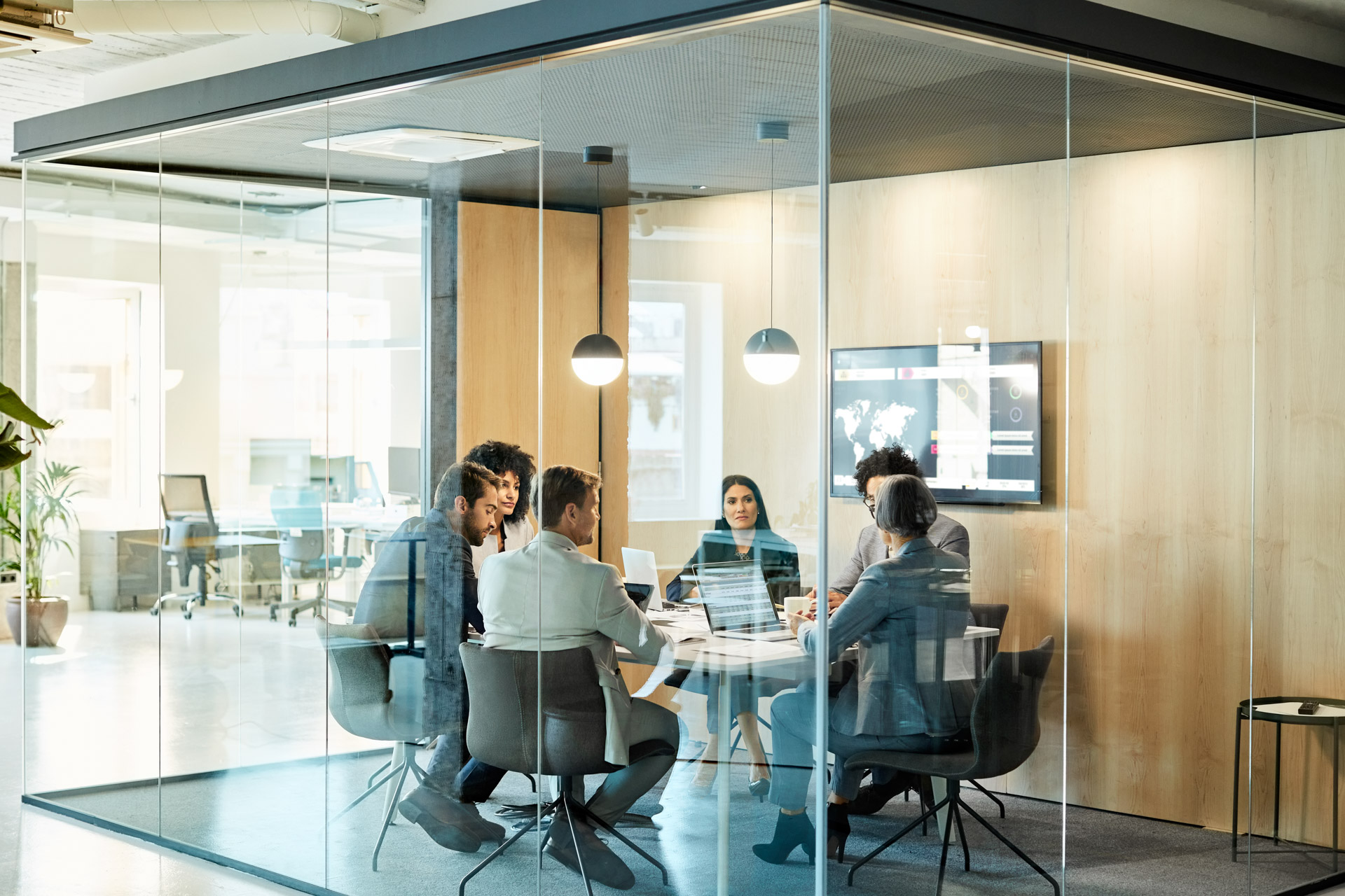 Business colleagues sitting at conference table seen through glass wall. Multi-ethnic coworkers are discussing in board room at office. They are planning strategy. | © Abel Mitjà Varela @getty